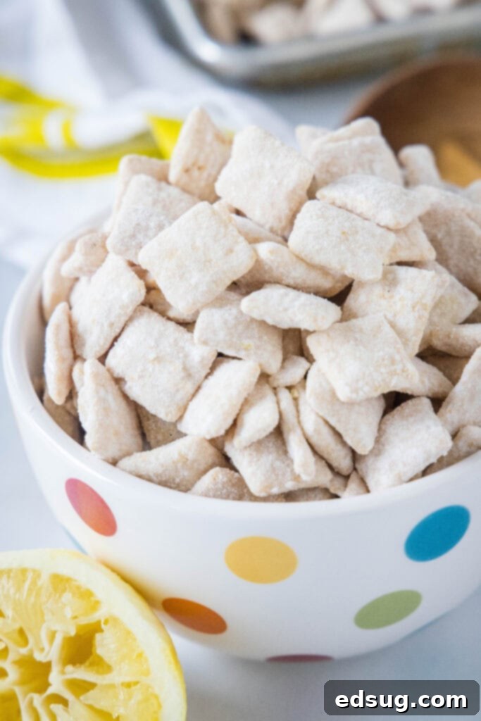 A beautiful close-up of a serving bowl filled with the finished lemon puppy chow, showcasing its light yellow hue and powdered sugar coating, ready to be enjoyed.