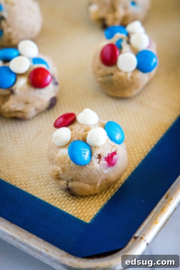 Red, White & Blue Cookies 4 Balls of 4th of July cookie dough topped with white chocolate chips and M&M's arranged on a baking sheet.