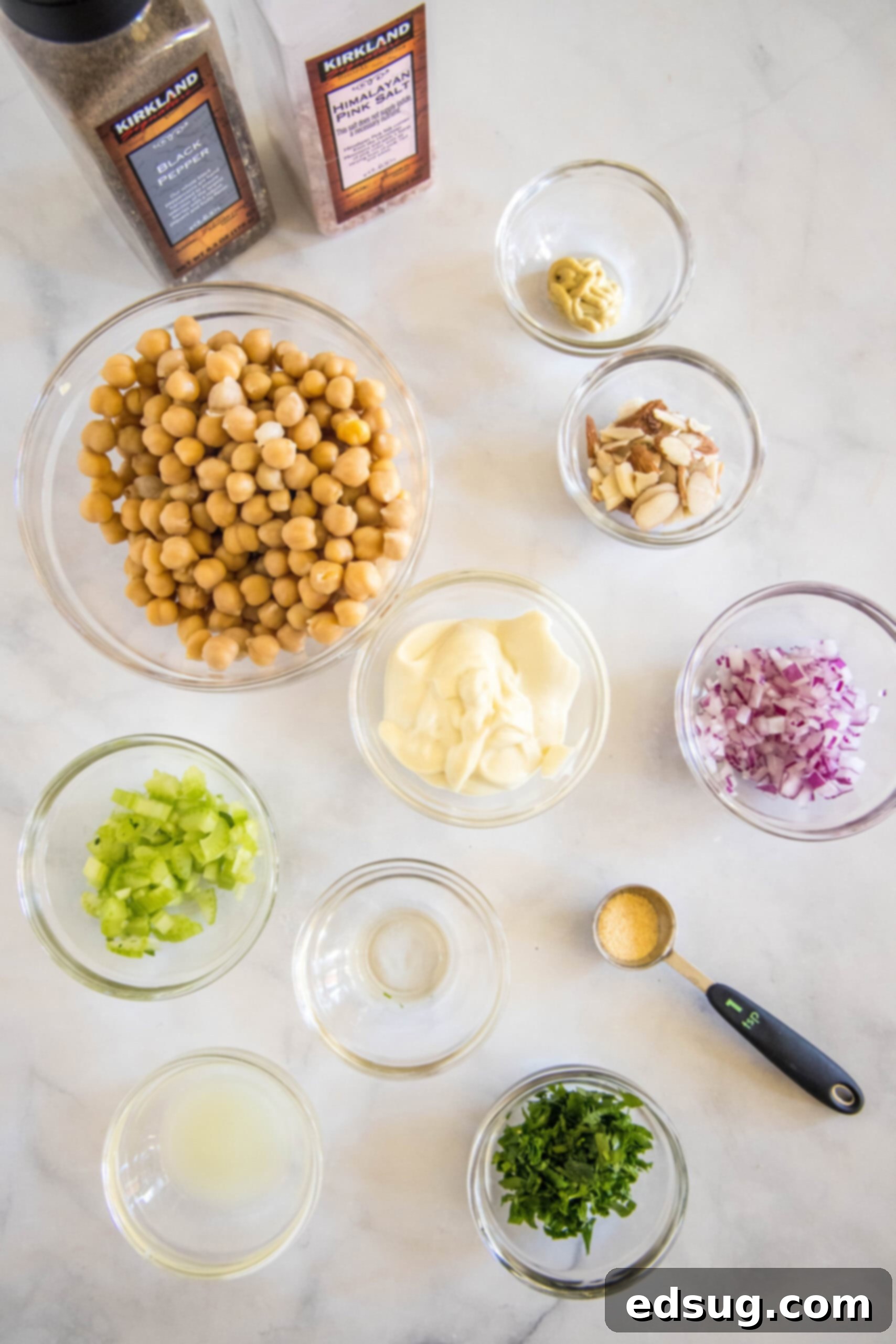 Fresh ingredients laid out for making chickpea chicken salad: a bowl of chickpeas, chopped celery, red onion, parsley, sliced almonds, and a selection of dressing ingredients.