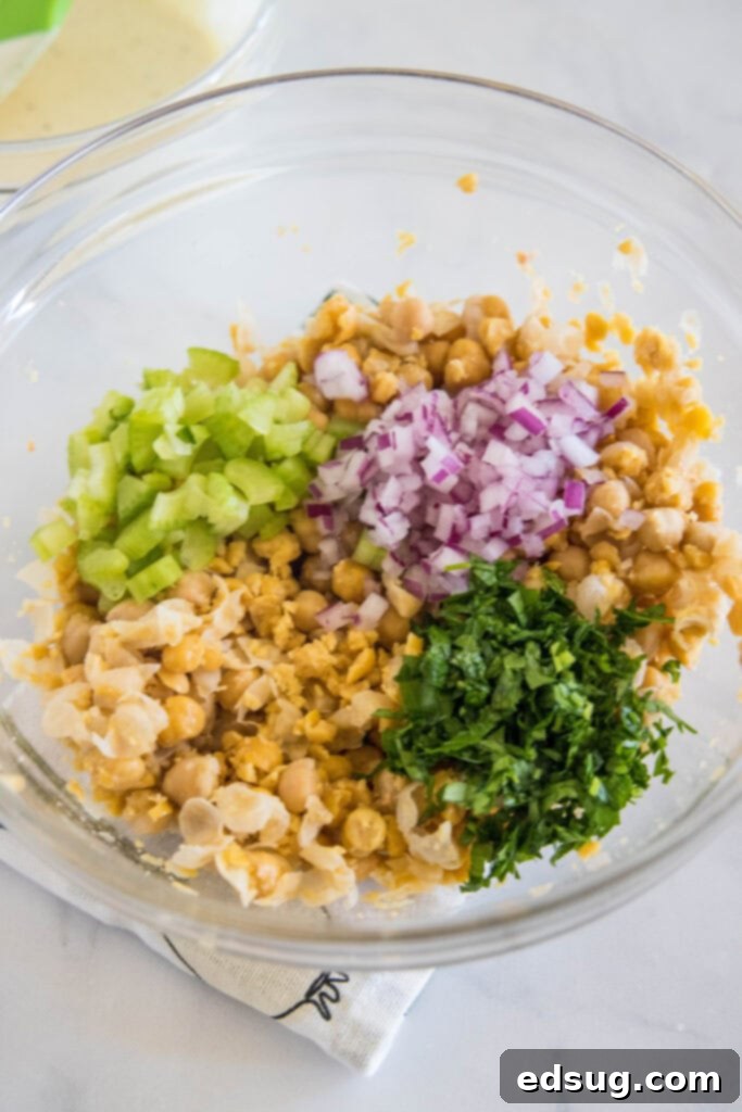 Drained and rinsed chickpeas partially mashed in a clear glass bowl, showcasing varying textures.