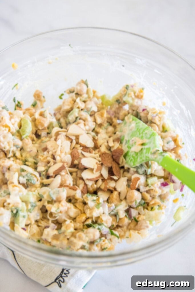 All chickpea chicken salad ingredients, including vegetables and dressing, stirred together in a glass bowl with a green serving spoon.
