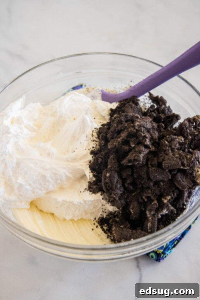 Prepare to be obsessed with Oreo fluff! Make this easy no-bake dessert with 5 ingredients in 5 minutes. It's perfect for dipping! Cool Whip and Oreos added to a bowl with whipped cream cheese.