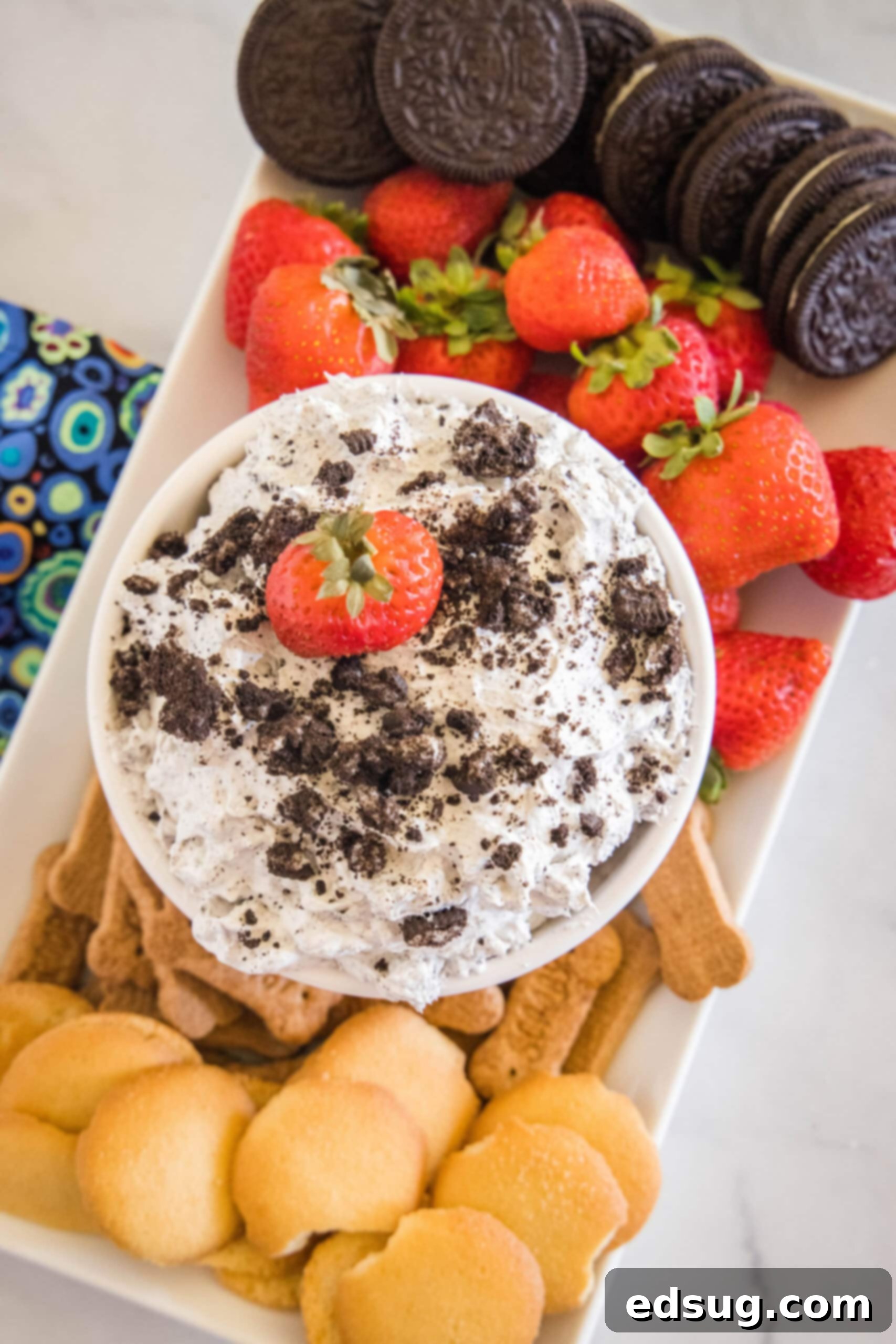 Prepare to be obsessed with Oreo fluff! Make this easy no-bake dessert with 5 ingredients in 5 minutes. It's perfect for dipping! Overhead view of a bowl of Oreo fluff topped with crushed Oreos and a strawberry, surrounded by a platter of dippables.