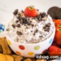 A bowl of Oreo fluff topped with crushed Oreos and a strawberry surrounded by a platter of dippables.
