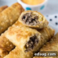 Crispy Cheeseburger Rolls 2 Close up of cheeseburger egg rolls stacked on a platter, with one egg roll broken in two and a bowl of dipping sauce in the background.