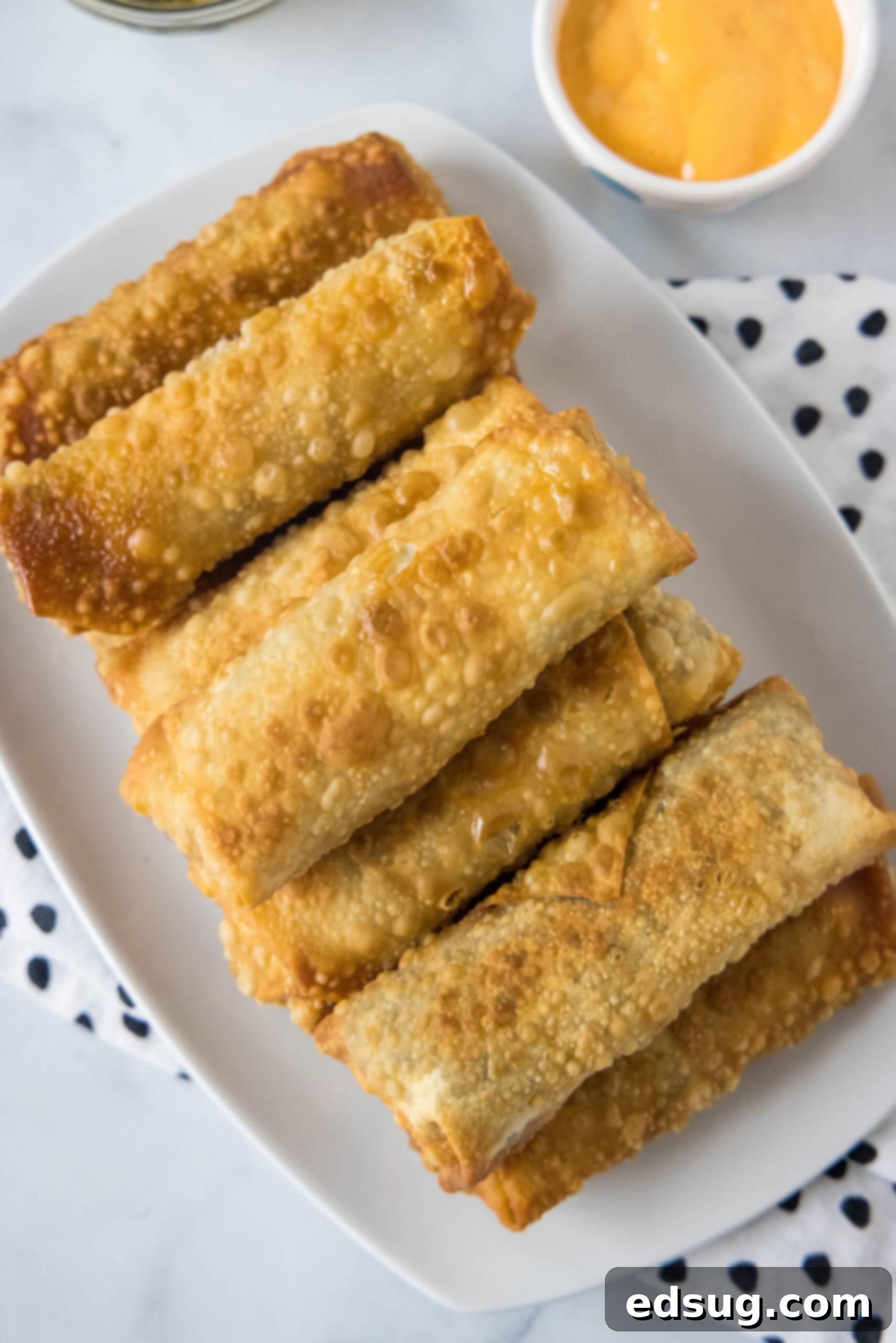 Looking for a fun and easy appetizer recipe? Try these cheeseburger egg rolls complete with creamy, tangy homemade burger sauce for dipping! Overhead view of cheeseburger egg rolls on a platter next to a bowl of dipping sauce.