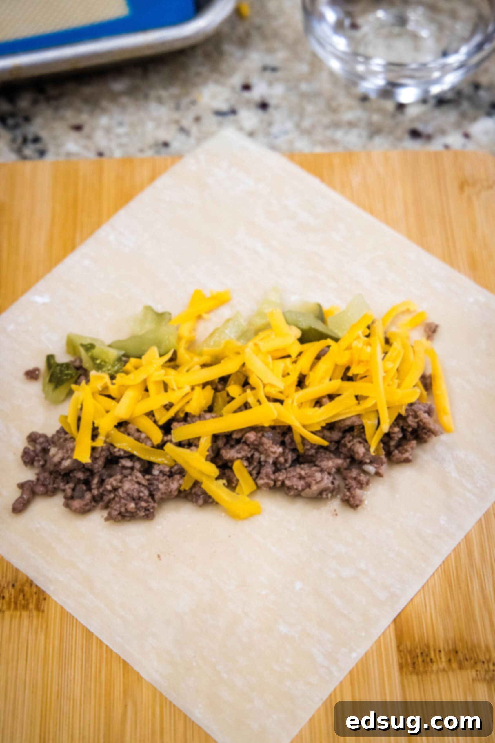 Looking for a fun and easy appetizer recipe? Try these cheeseburger egg rolls complete with creamy, tangy homemade burger sauce for dipping! Cheeseburger filling topped with shredded cheese on top of an egg roll wrapper.