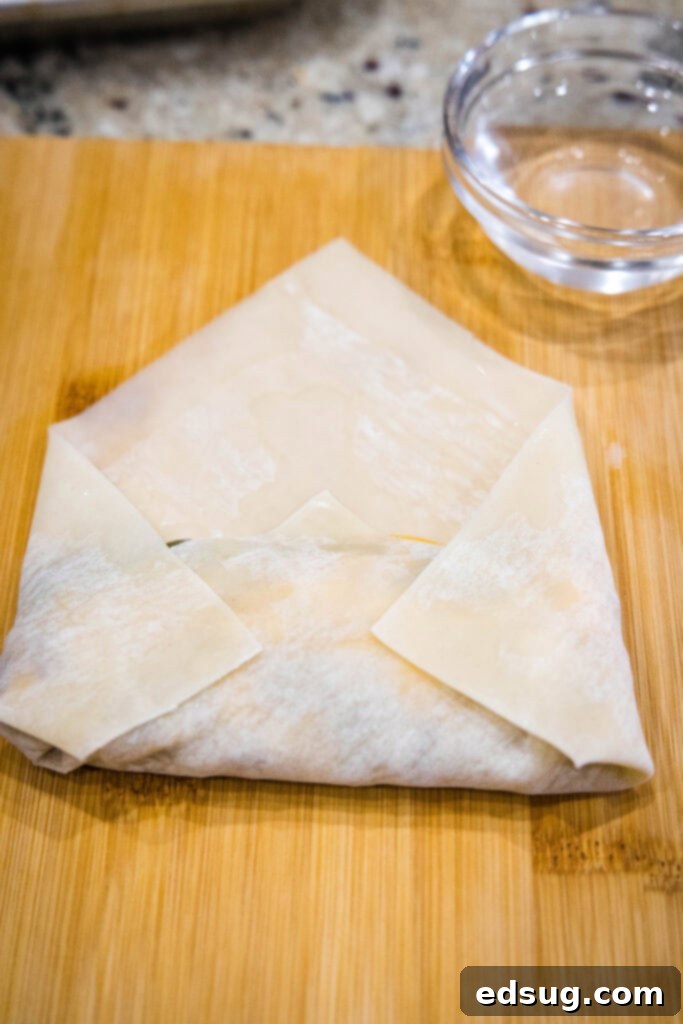 Looking for a fun and easy appetizer recipe? Try these cheeseburger egg rolls complete with creamy, tangy homemade burger sauce for dipping! A partially folded cheeseburger egg roll on a wooden surface.