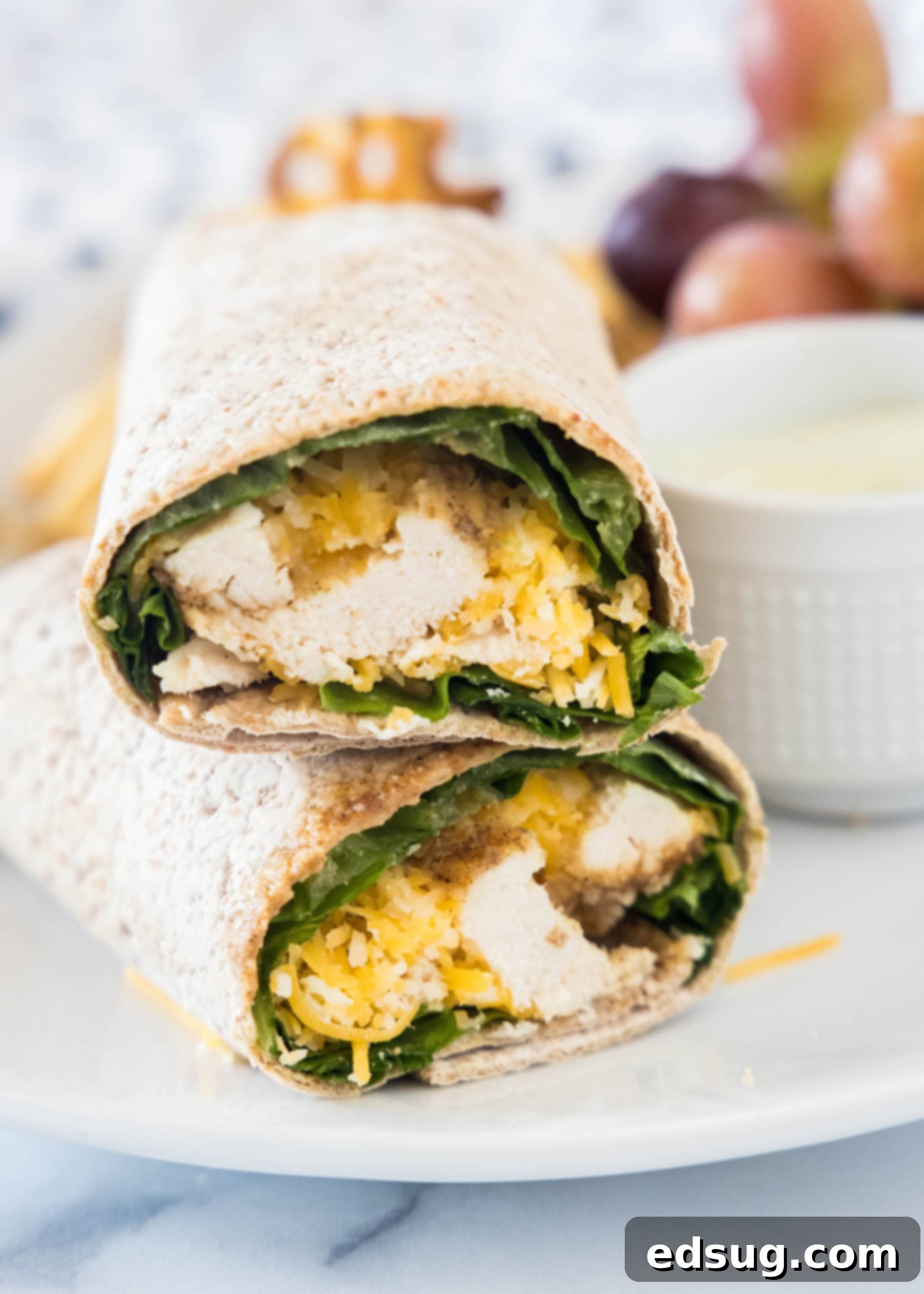 This easy Chick Fil A Cool Wrap recipe is the best excuse to skip the drive-thru! Enjoy this copycat at home with your favorite dipping sauce. Two halves of a Chick Fil A Cool Wrap stacked on a plate next to a bowl of dipping sauce.