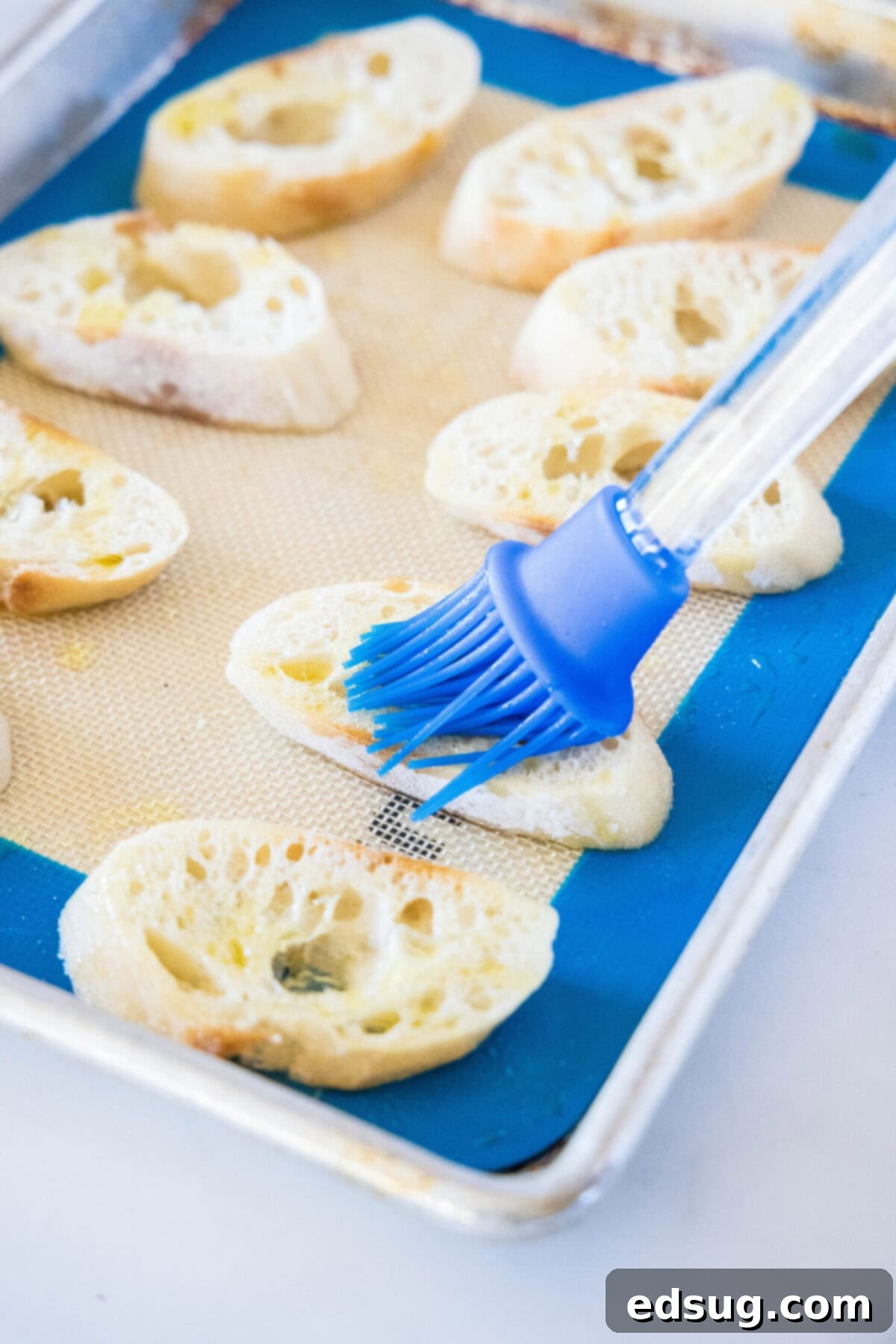 This easy bruschetta is the perfect appetizer or party food. It's loaded with tomatoes, garlic, and basil, and only takes 5 minutes. Slices of baguette on a silicone mat on a baking sheet, with a kitchen brush putting olive oil on them