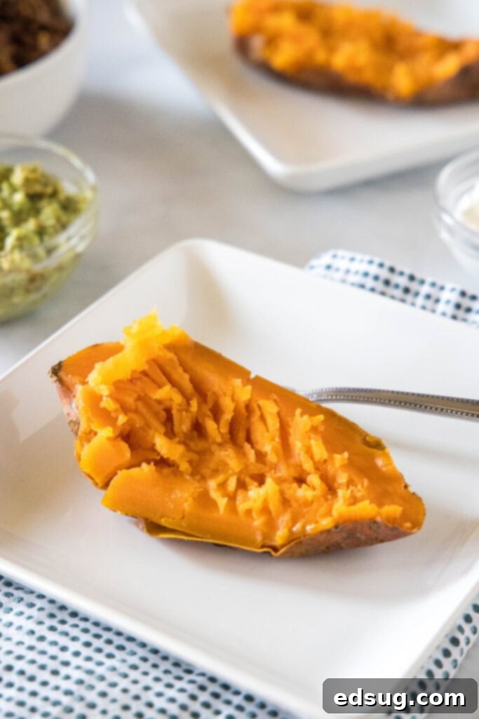 These taco stuffed sweet potatoes are soft and fluffy sweet potatoes piled high with savory ground beef and your favorite taco toppings! One half of a cooked sweet potato with the flesh fluffed on a white plate next to a fork.
