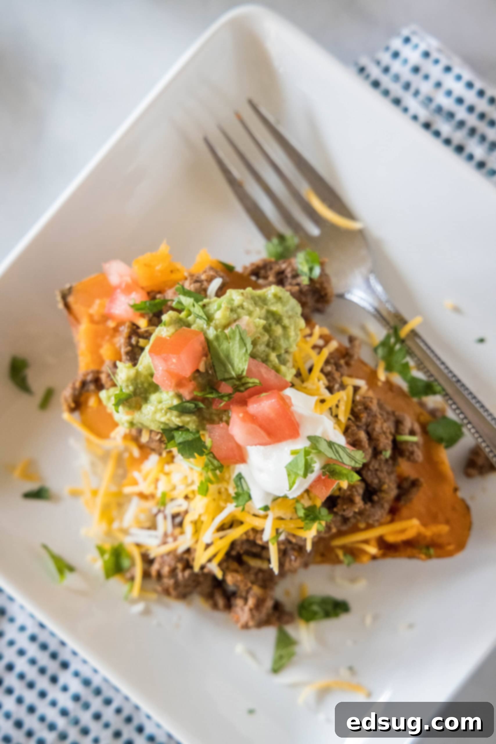 These taco stuffed sweet potatoes are soft and fluffy sweet potatoes piled high with savory ground beef and your favorite taco toppings! Overhead view of a taco sweet potato piled with taco toppings served on a white plate.