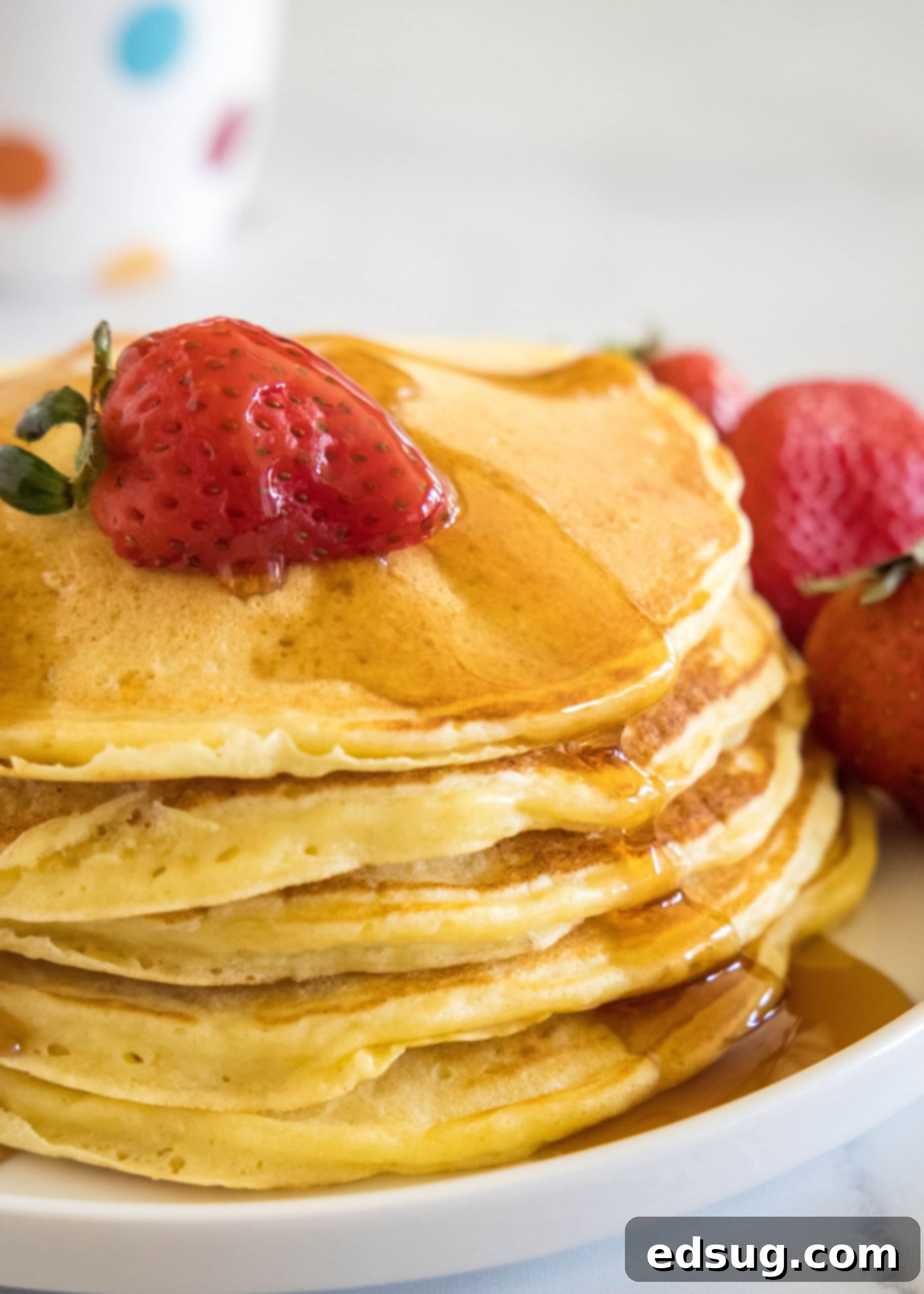 Ricotta pancakes are extra soft, fluffy, and so flavorful! Top these with syrup and a squeeze of lemon for the ultimate breakfast treat! A stack of ricotta pancakes topped with a strawberry and maple syrup on a plate, next to more fresh strawberries.