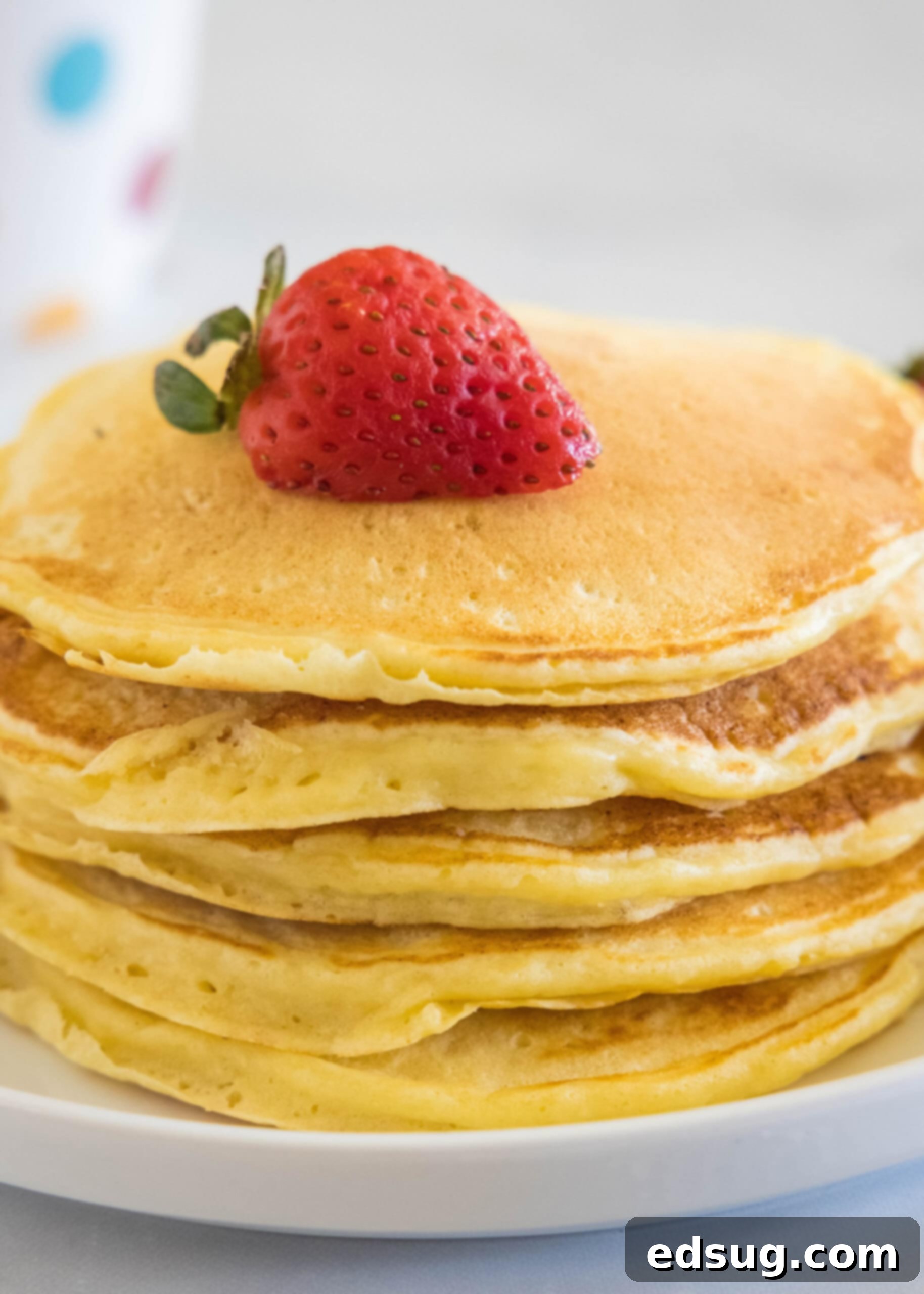 Ricotta pancakes are extra soft, fluffy, and so flavorful! Top these with syrup and a squeeze of lemon for the ultimate breakfast treat! A stack of ricotta pancakes topped with a strawberry a plate.