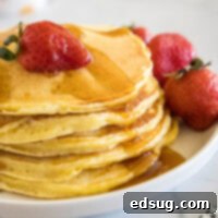 Fluffy Ricotta Pancakes 2 A stack of ricotta pancakes topped with a strawberry and maple syrup on a plate, next to more fresh strawberries.