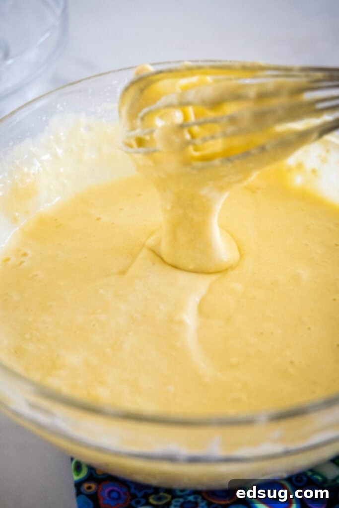 Ricotta pancakes are extra soft, fluffy, and so flavorful! Top these with syrup and a squeeze of lemon for the ultimate breakfast treat! A whisk dripping ricotta pancake batter into a glass bowl.