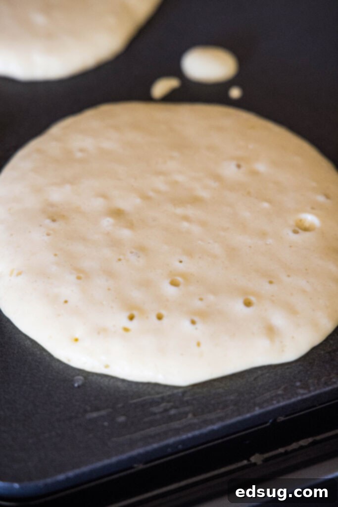 Ricotta pancakes are extra soft, fluffy, and so flavorful! Top these with syrup and a squeeze of lemon for the ultimate breakfast treat! Ricotta pancake batter cooking on a griddle, showing small bubbles on the surface to indicate that it's ready to flip.