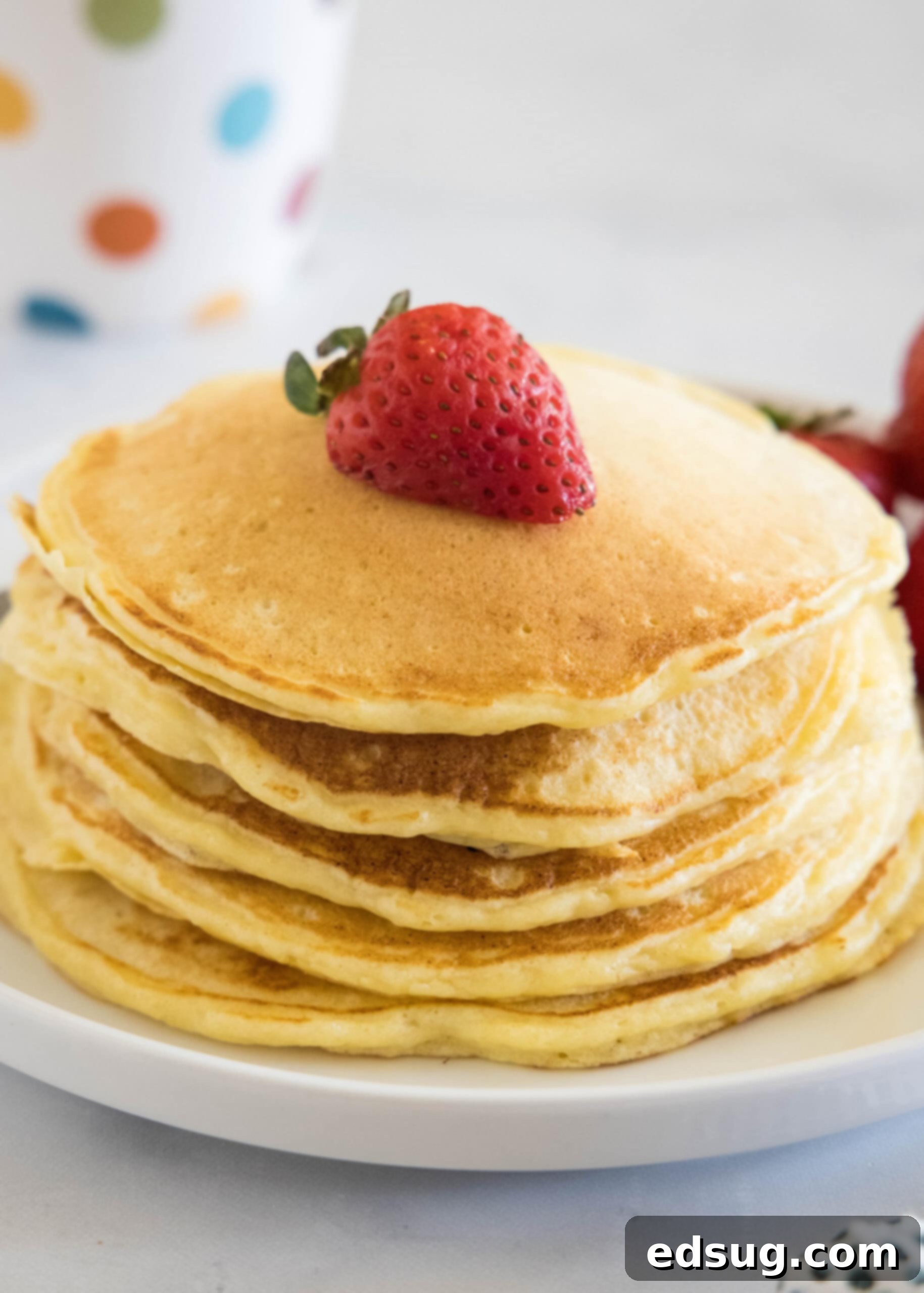 Ricotta pancakes are extra soft, fluffy, and so flavorful! Top these with syrup and a squeeze of lemon for the ultimate breakfast treat! A stack of ricotta pancakes topped with a strawberry a plate.