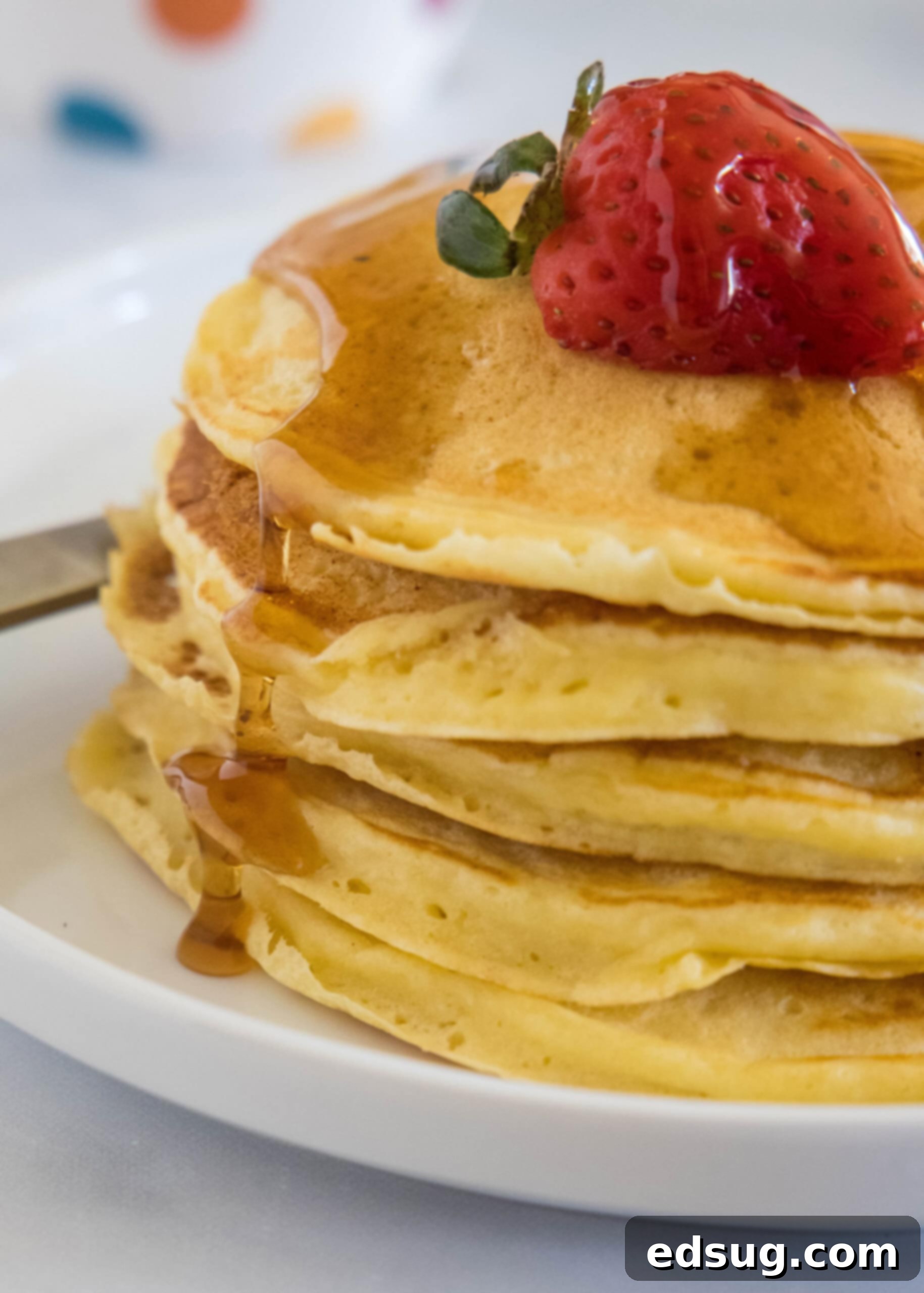 Ricotta pancakes are extra soft, fluffy, and so flavorful! Top these with syrup and a squeeze of lemon for the ultimate breakfast treat! A stack of ricotta pancakes topped with a strawberry and maple syrup on a plate.