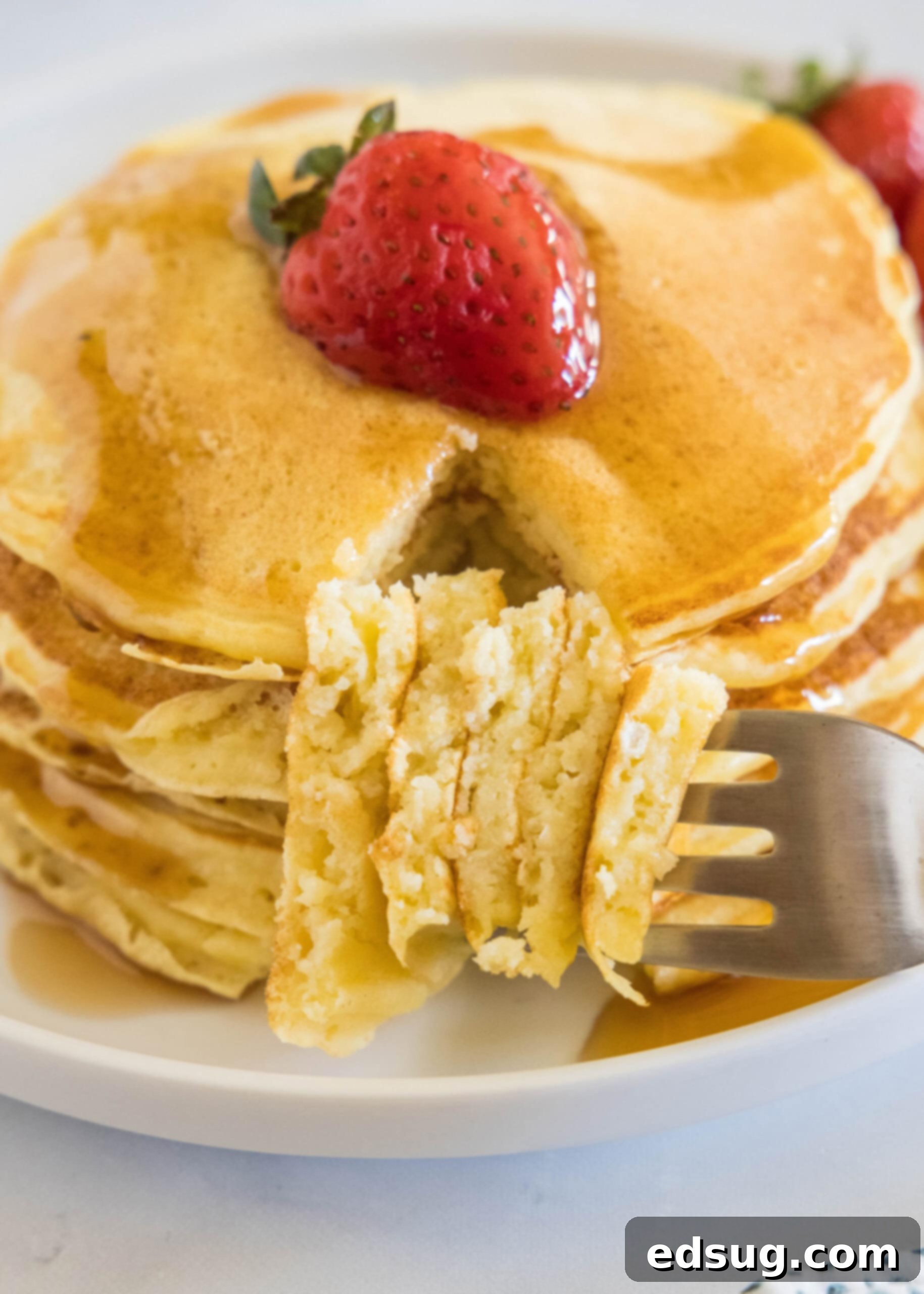 Ricotta pancakes are extra soft, fluffy, and so flavorful! Top these with syrup and a squeeze of lemon for the ultimate breakfast treat! A forkful laying next stack of ricotta pancakes topped with a strawberry and maple syrup on a plate.