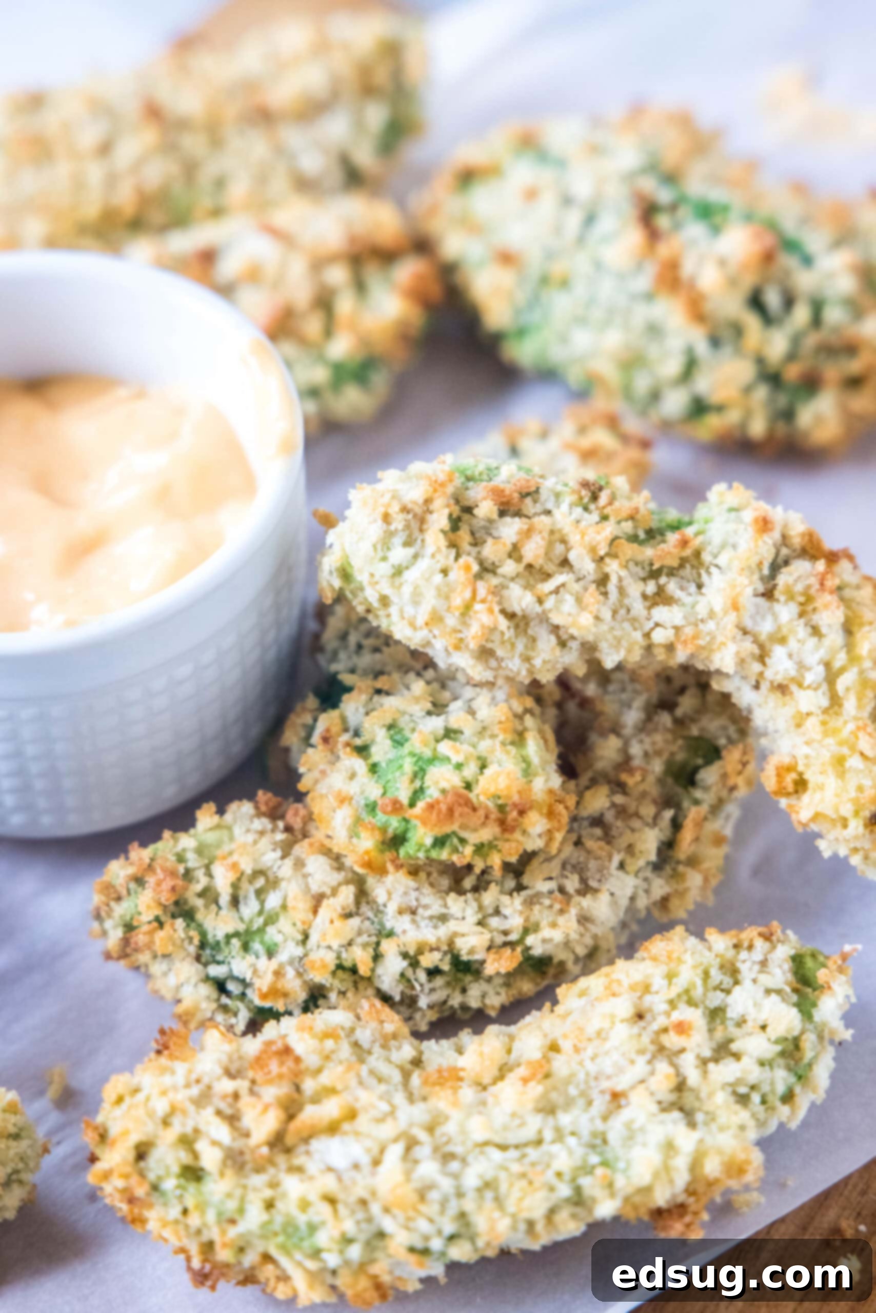 Avocado fries are crispy on the outside and warm and creamy on the inside, made in the air fryer (or oven). Don't forget the dipping sauce! Crispy avocado fries served on a wooden cutting board with parchment paper, accompanied by a small bowl of dipping sauce.