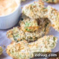 Crispy Avocado Fries 2 Avocado fries on a wooden cutting board lined with parchment paper, next to a small bowl of dipping sauce.