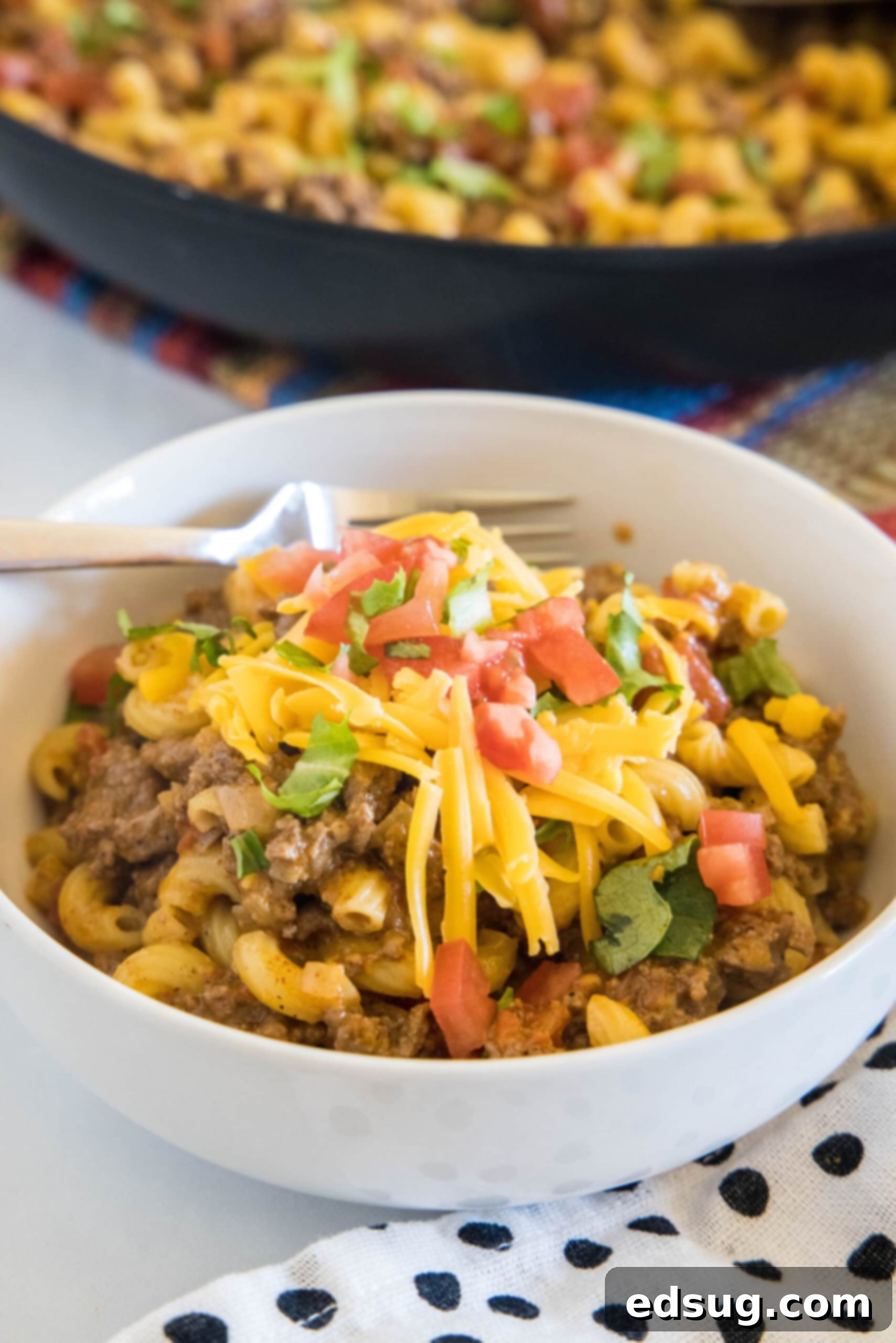 A bowl of creamy, cheesy taco mac and cheese with a skillet in the background, garnished with fresh cilantro.