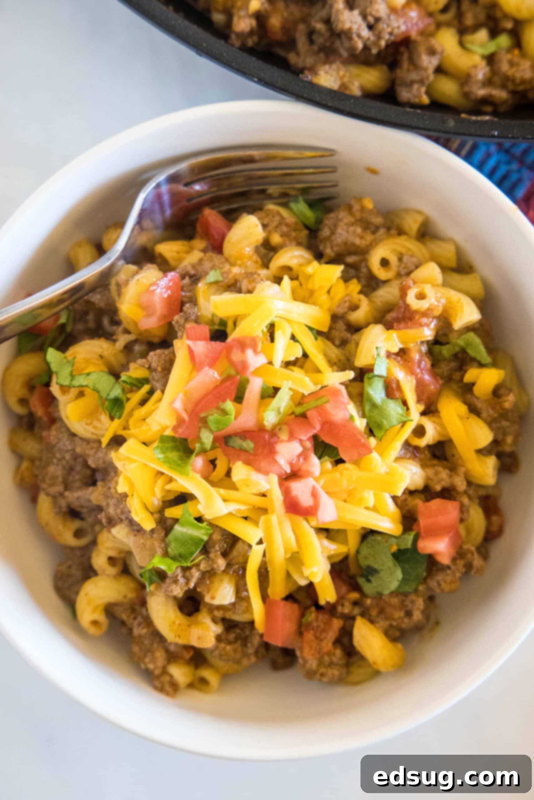 Overhead view of a bowl of taco mac and cheese with a fork, garnished with fresh cilantro and a dollop of sour cream.