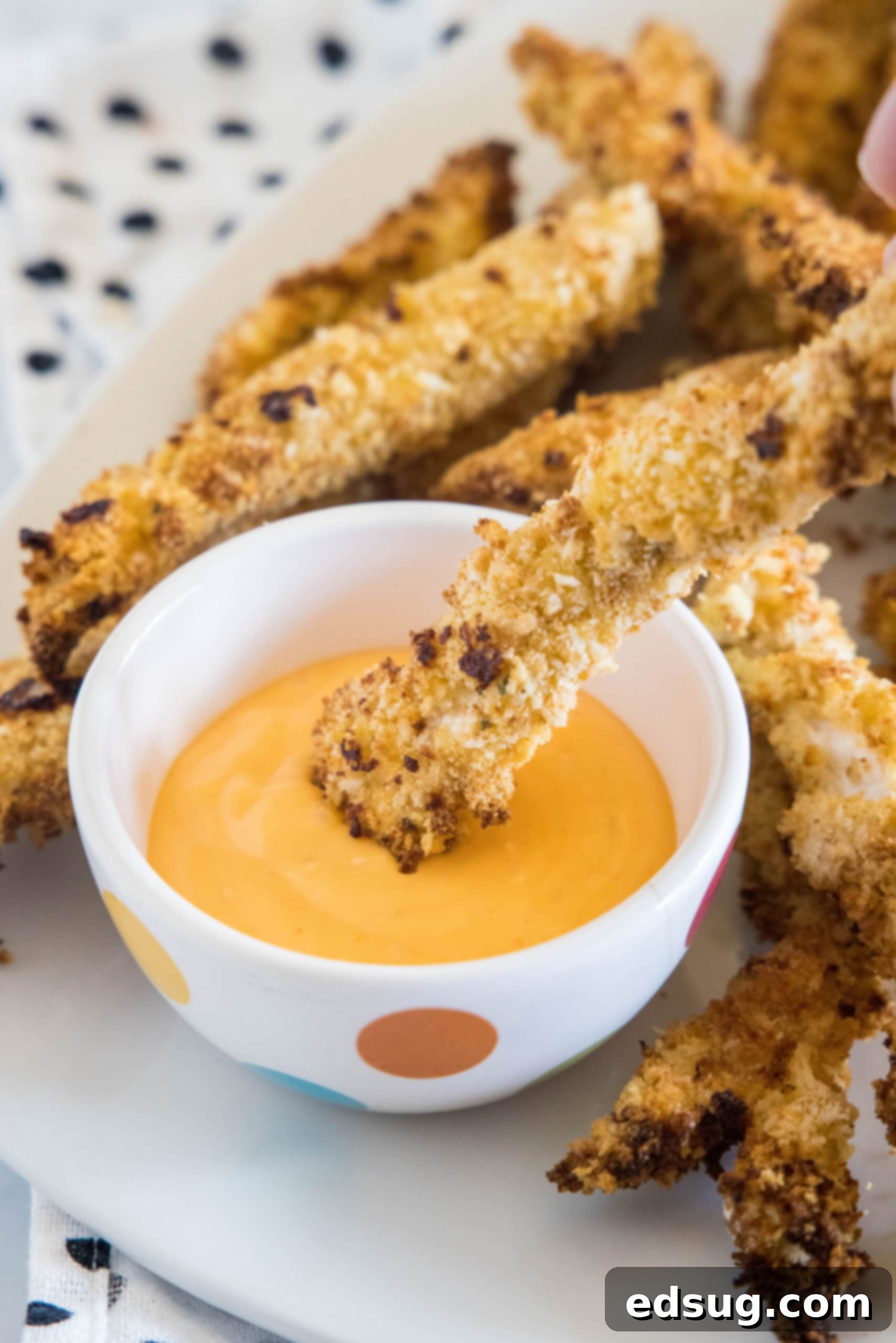 Juicy on the inside and crunchy on the outside, chicken fries are a seriously addictive appetizer or side. Ready for dipping in 20 minutes! A chicken fry being dipped into a small bowl of dipping sauce, surrounded by more chicken fries on a platter.