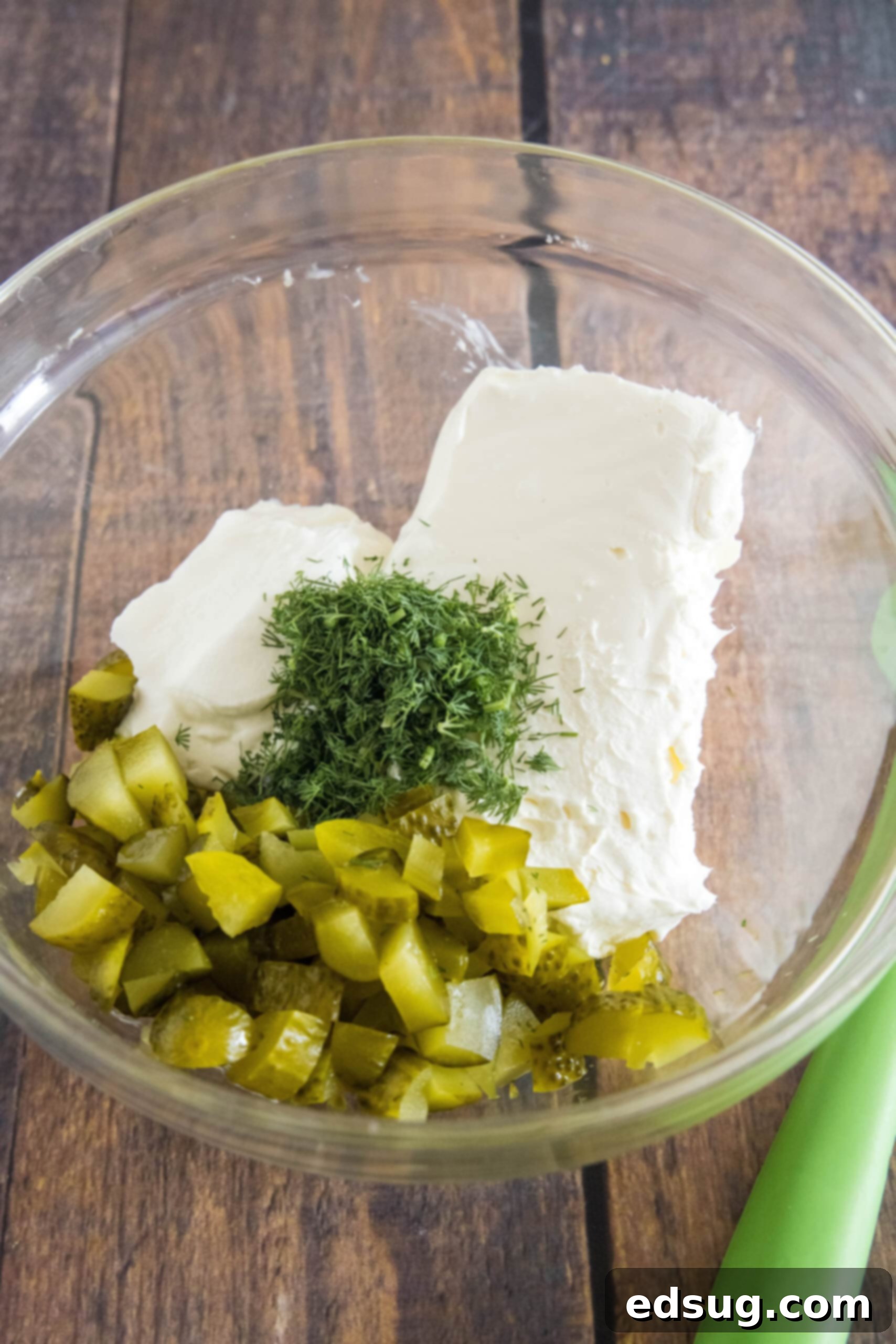 Creamy dill pickle dip is briny, cool, and crunchy. Made with 5 ingredients in minutes, it's delicious for dipping just about everything! Dill pickle dip ingredients fully combined in a clear glass mixing bowl.
