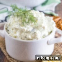 Creamy Dill Pickle Dip 2 Pickle dip topped with fresh dill sprigs in a white serving dish, with a bowl of chips in the background.