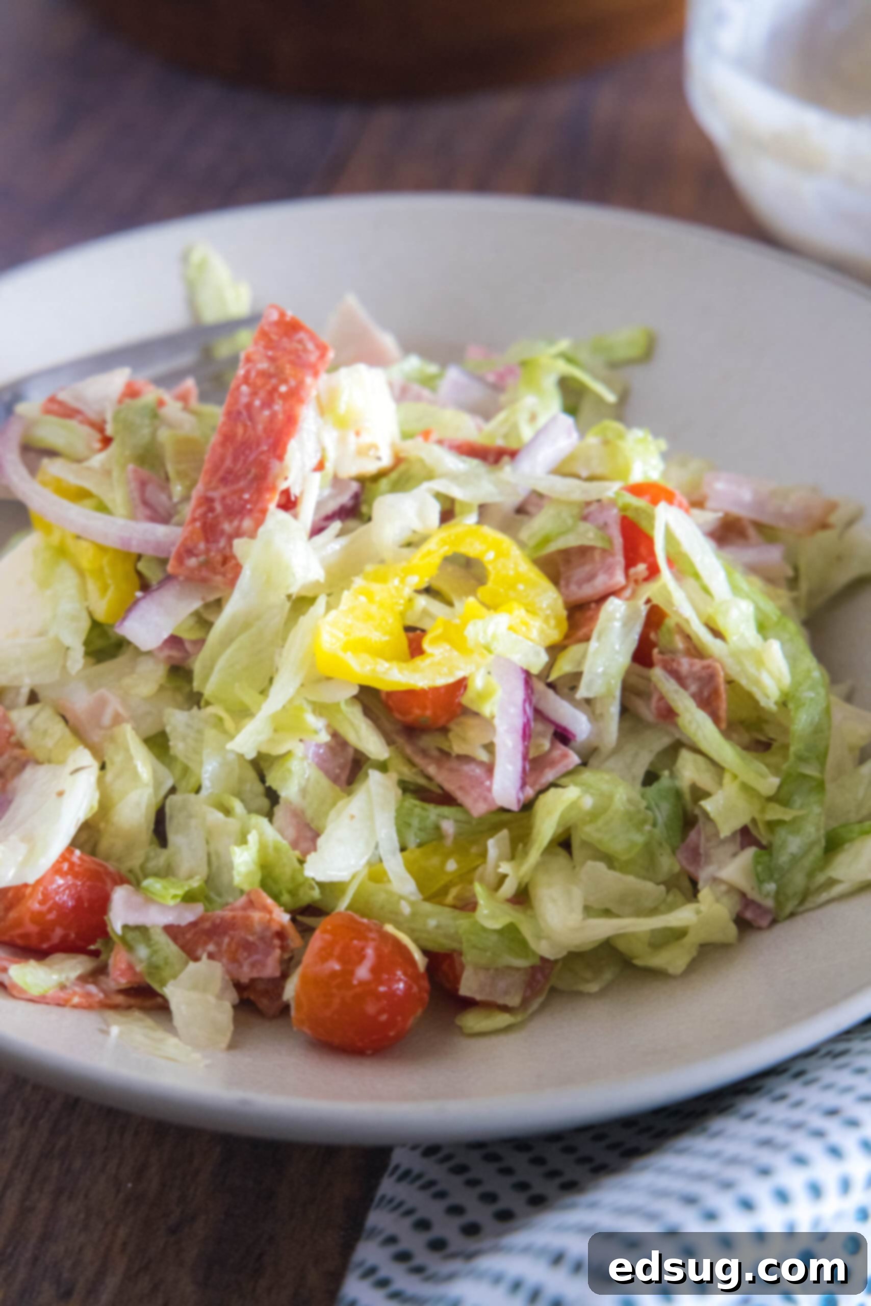 A large white bowl filled with a vibrant grinder salad, showcasing crisp lettuce, colorful tomatoes, and various deli meats.