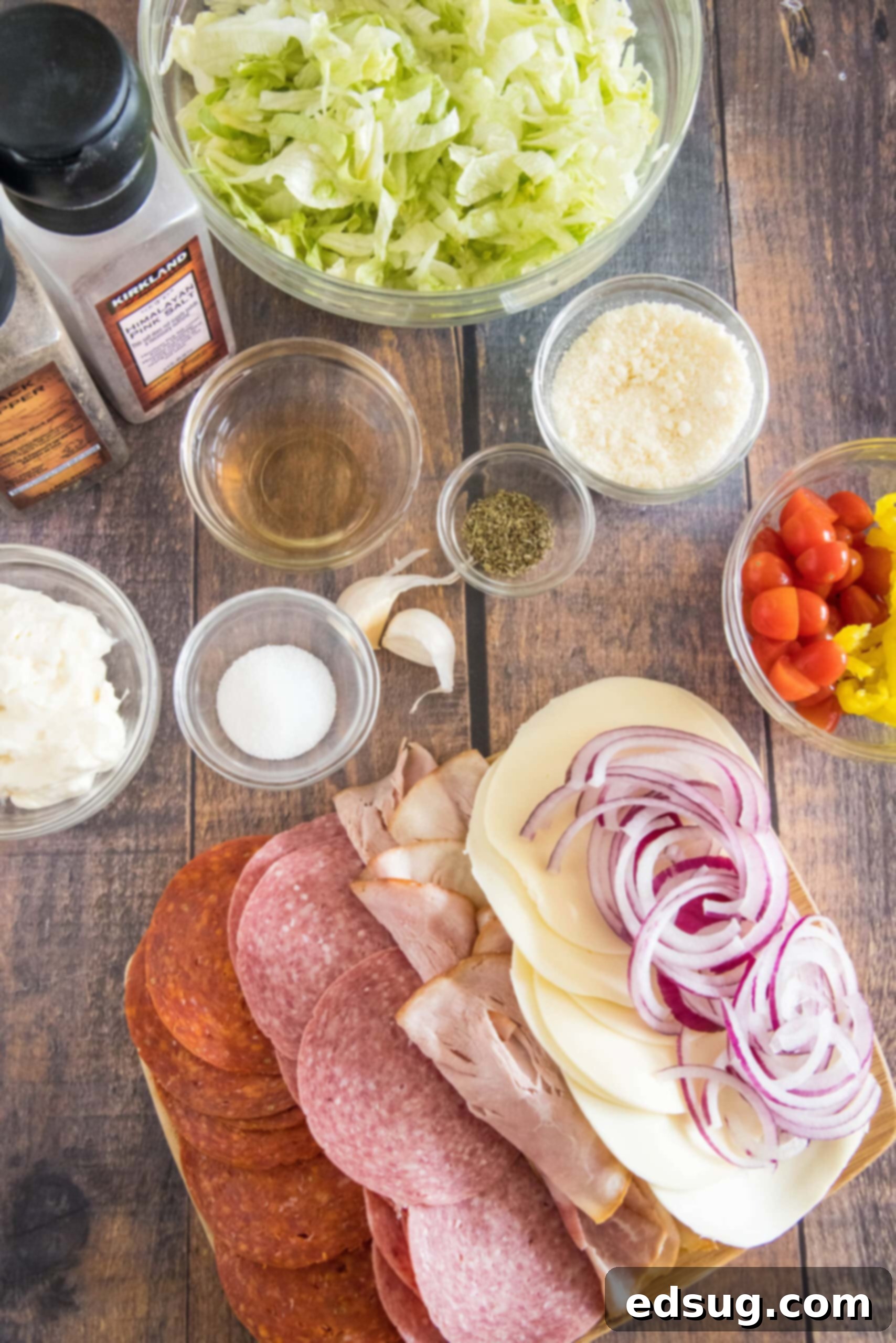 A selection of fresh ingredients laid out, including lettuce, tomatoes, red onion, deli meats, and cheese, ready for the grinder salad.