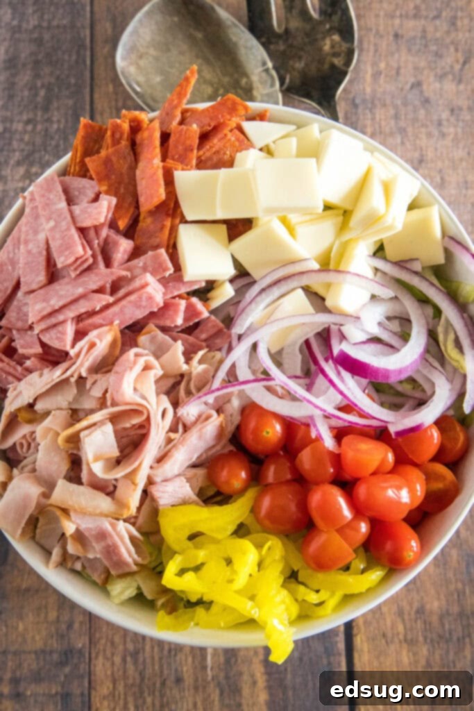 An overhead view of a large bowl filled with various grinder salad ingredients – chopped lettuce, meats, cheese, and vegetables – before dressing.