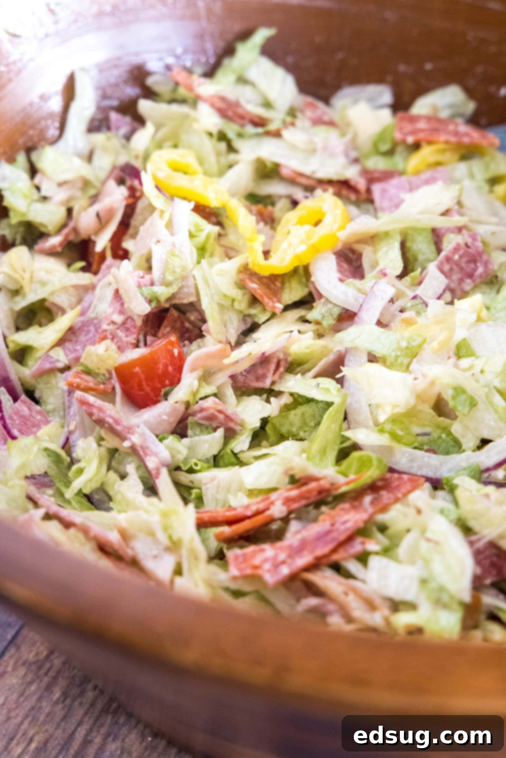 Grinder salad fully tossed with dressing in a rustic wooden bowl, ready to be enjoyed.