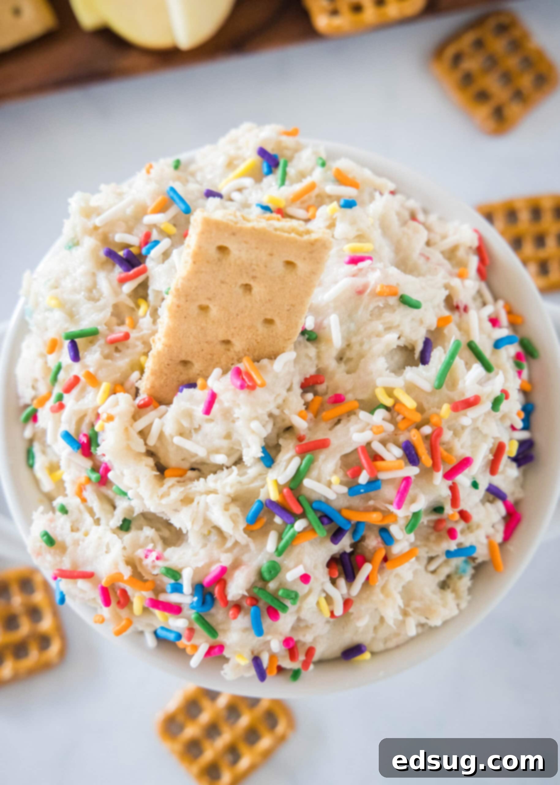 Overhead view of cake batter dip in a white bowl with a cookie stuck into the top. Overhead view of cake batter dip in a white bowl with a cookie stuck into the top.