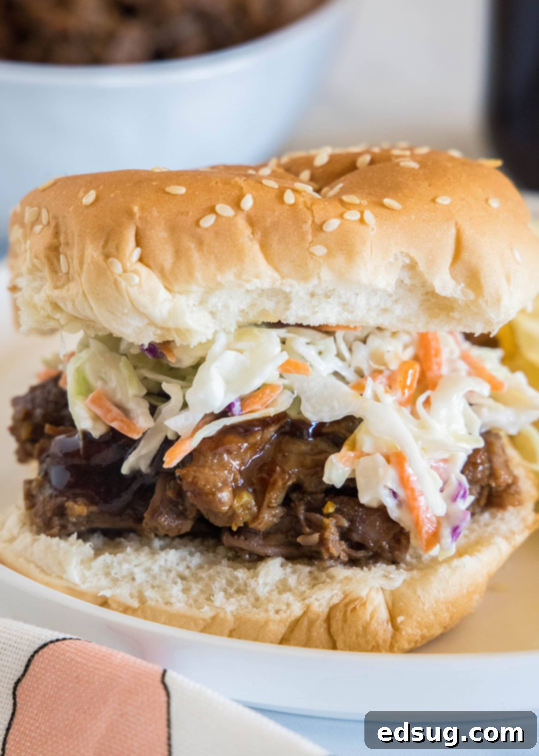 A BBQ beef sandwich with coleslaw on a white plate, showcasing tender shredded beef.