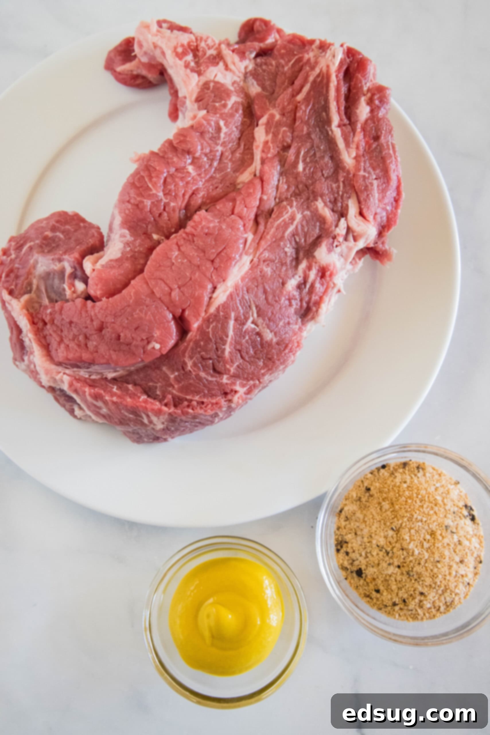 Ingredients for slow cooker BBQ beef laid out: chuck roast, mustard, dry rub, and barbecue sauce.