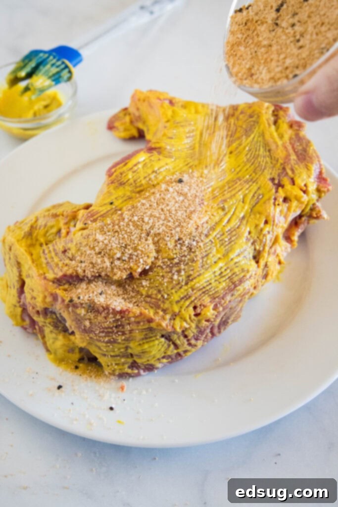 Chuck roast coated with mustard and dry rub on a white plate, ready for the slow cooker.