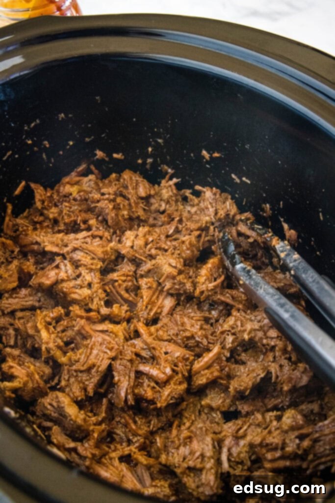 Shredding tender BBQ beef with two forks inside the crock pot, before adding sauce.