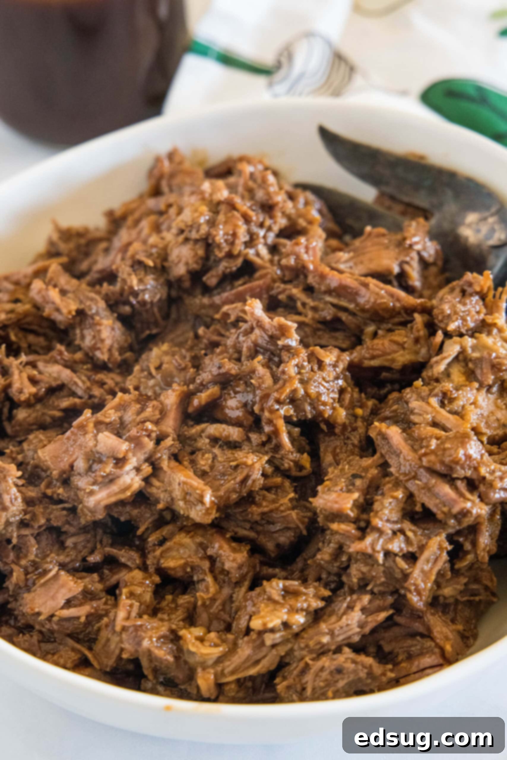 Metal tongs gently lifting a portion of shredded BBQ beef, showing its tender texture.