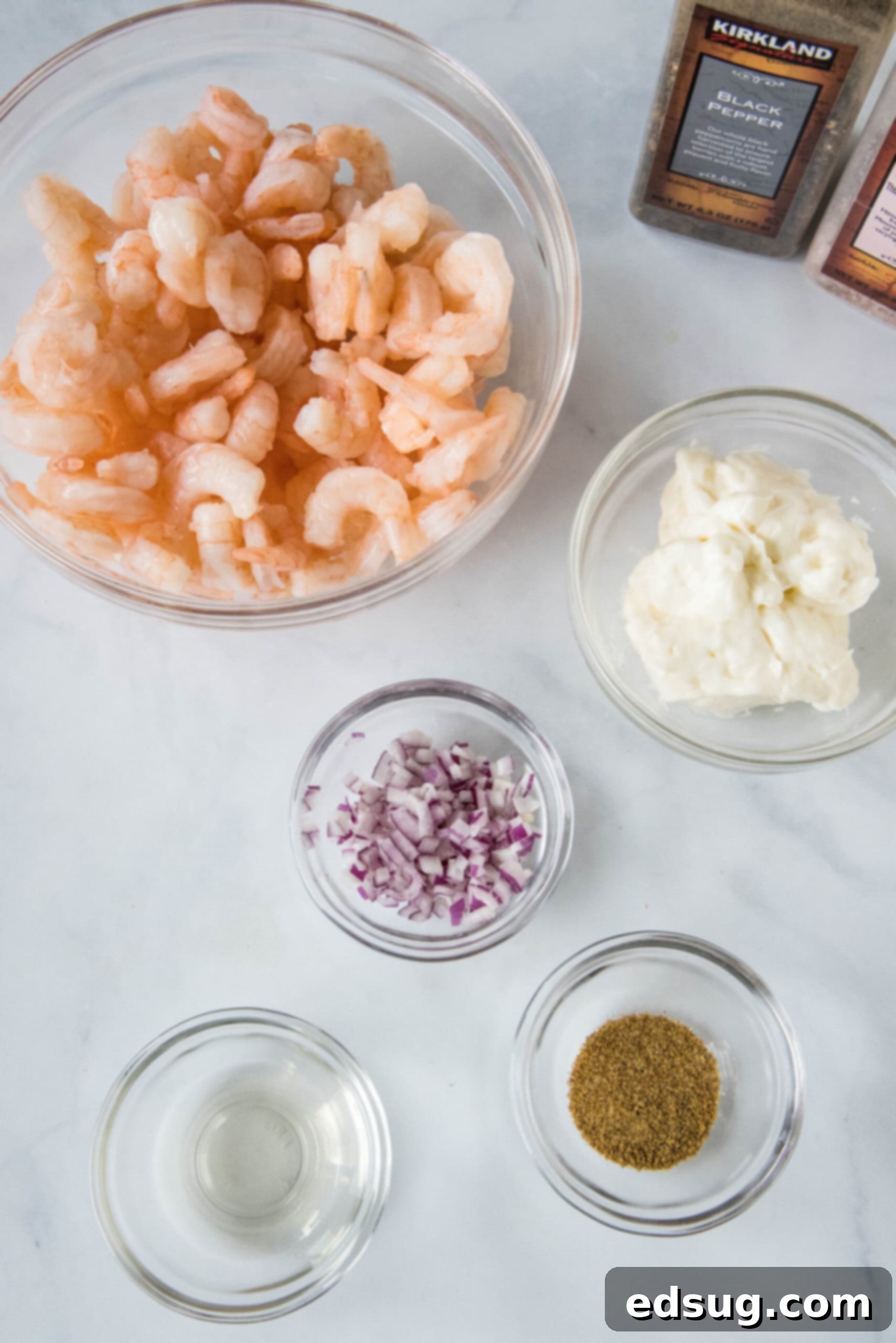 This creamy shrimp salad is about to become your favorite summer recipe! Made with chilled shrimp, crisp red onion, and Old Bay seasoning. Ingredients for shrimp salad laid out on a kitchen counter, including shrimp, red onion, mayonnaise, vinegar, and Old Bay seasoning.