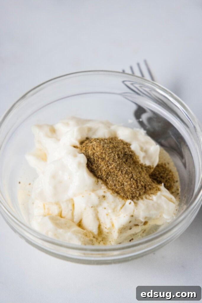 This creamy shrimp salad is about to become your favorite summer recipe! Made with chilled shrimp, crisp red onion, and Old Bay seasoning. Shrimp salad dressing ingredients combined in a glass bowl, showing the creamy texture before adding shrimp.