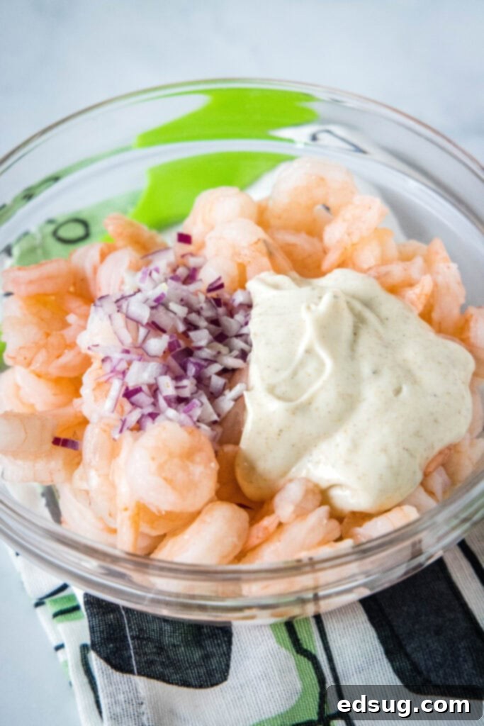 This creamy shrimp salad is about to become your favorite summer recipe! Made with chilled shrimp, crisp red onion, and Old Bay seasoning. Shrimp, creamy dressing, and diced onions combined in a glass bowl, ready to be tossed for the salad.