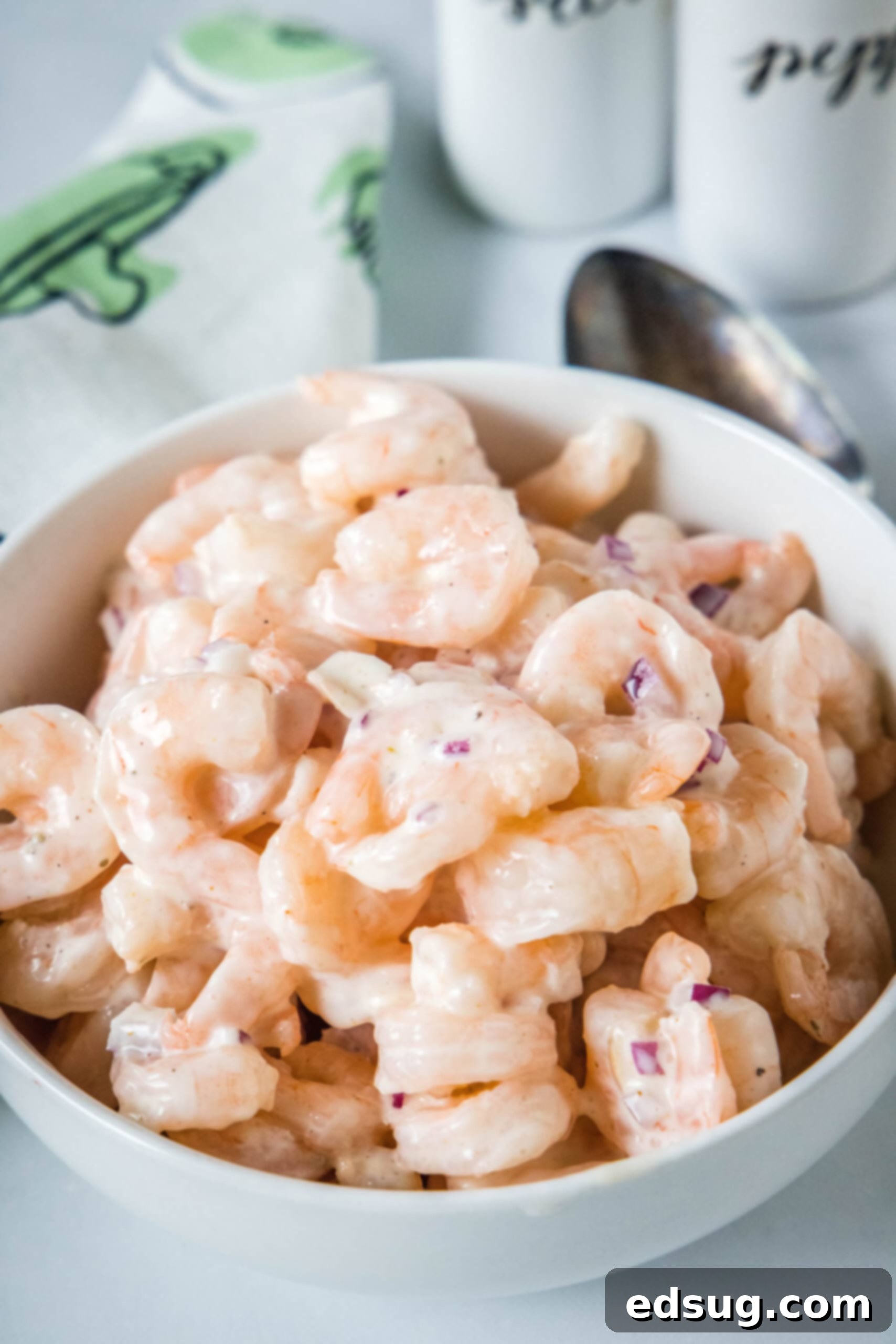 This creamy shrimp salad is about to become your favorite summer recipe! Made with chilled shrimp, crisp red onion, and Old Bay seasoning. Shrimp salad in a serving bowl with a spoon resting inside, ready to be enjoyed.