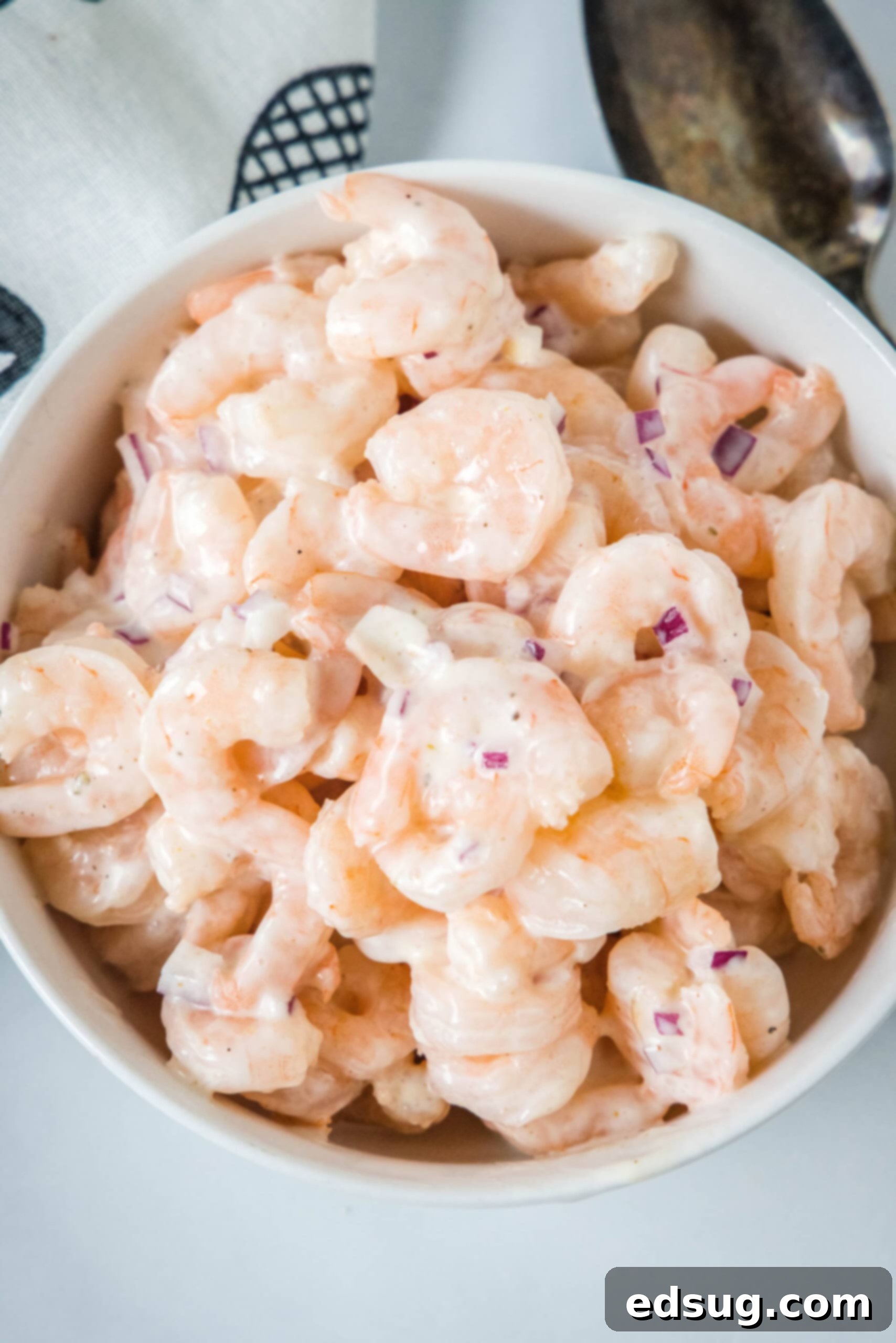 This creamy shrimp salad is about to become your favorite summer recipe! Made with chilled shrimp, crisp red onion, and Old Bay seasoning. Overhead view of shrimp salad in a white bowl, garnished with fresh herbs.