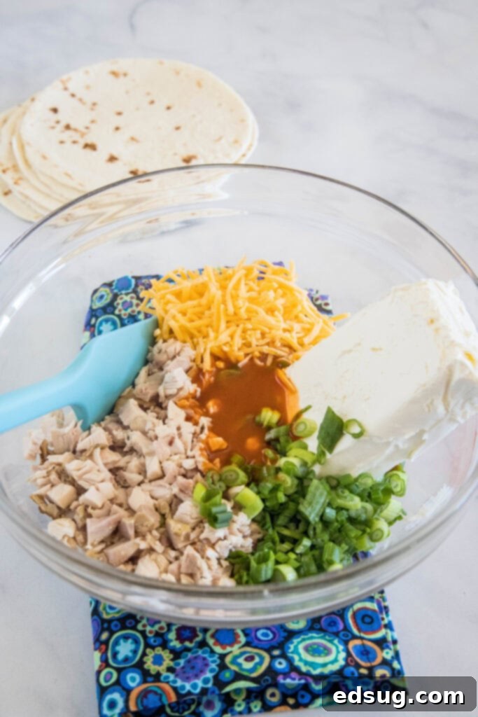 Buffalo chicken pinwheels are a quick and easy appetizer packed with bold Buffalo flavor. Roll up the spicy chicken filling, chill, and slice! All the delicious ingredients for the Buffalo chicken filling perfectly combined in a clear glass bowl, showcasing a creamy, orange-hued mixture.