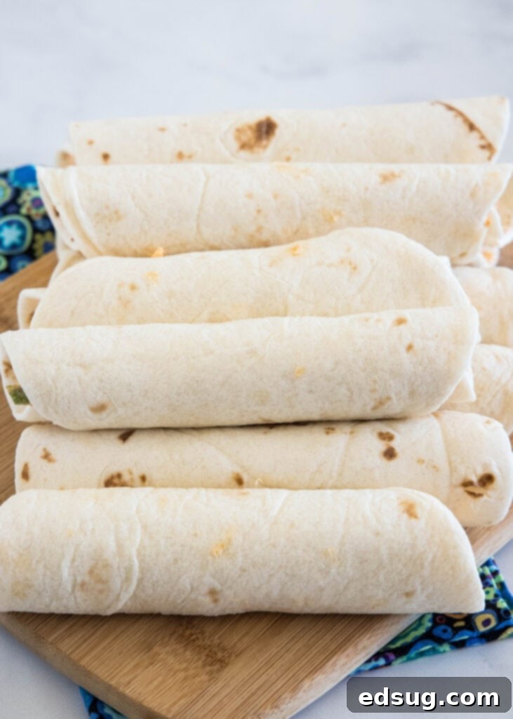 Buffalo chicken pinwheels are a quick and easy appetizer packed with bold Buffalo flavor. Roll up the spicy chicken filling, chill, and slice! Several tightly rolled Buffalo chicken tortillas neatly stacked on a wooden cutting board, prepped for chilling.