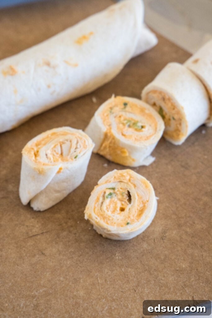Buffalo chicken pinwheels are a quick and easy appetizer packed with bold Buffalo flavor. Roll up the spicy chicken filling, chill, and slice! A vibrant display of freshly sliced Buffalo chicken pinwheels alongside a whole rolled tortilla, highlighting the distinct spiral pattern and appealing colors.
