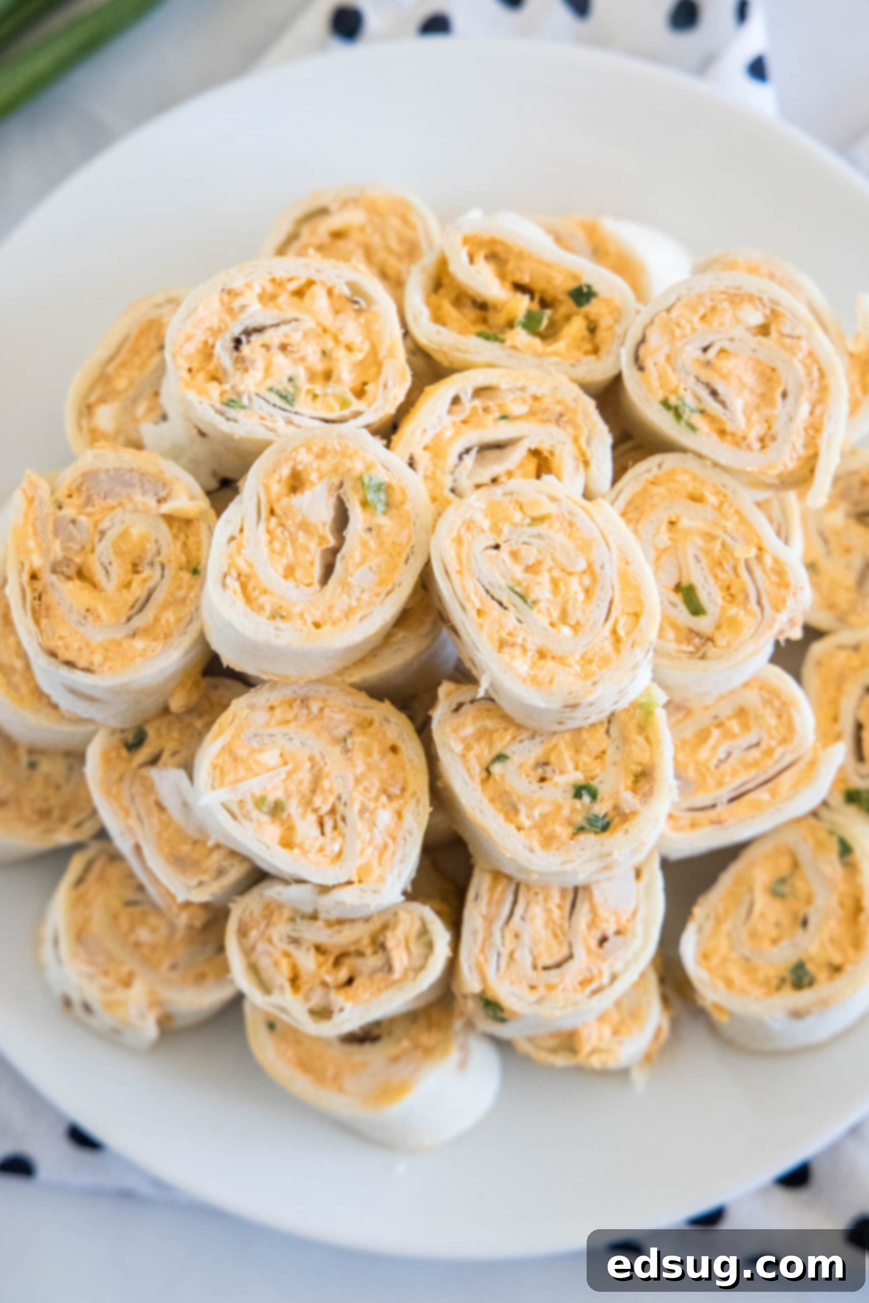 Buffalo chicken pinwheels are a quick and easy appetizer packed with bold Buffalo flavor. Roll up the spicy chicken filling, chill, and slice! An inviting overhead view of perfectly sliced Buffalo chicken pinwheels, expertly arranged on a white serving plate, promising a delightful culinary experience.